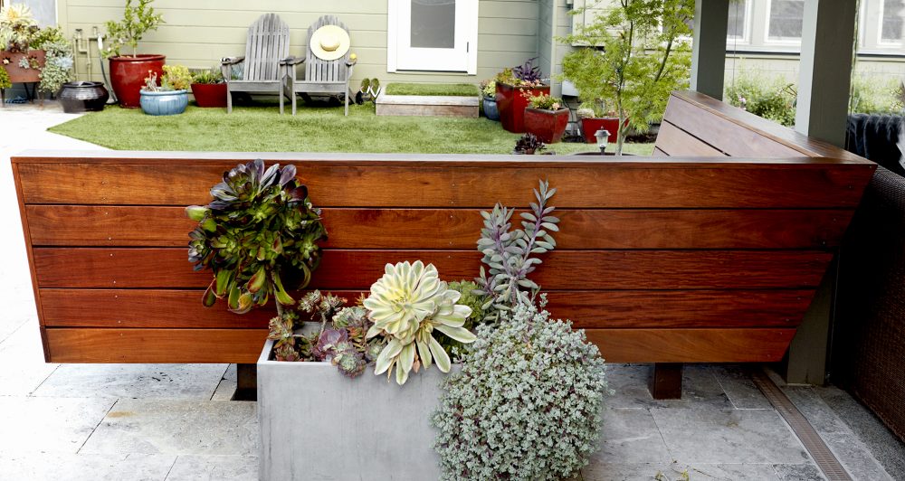 Yard view of back of L shaped built-in bench showing five long dark stained polished wood panels