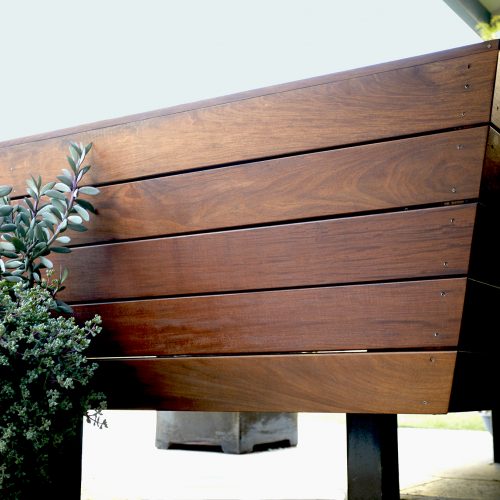 Corner of L shaped, dark stained, polished wooden built-in bench from the back