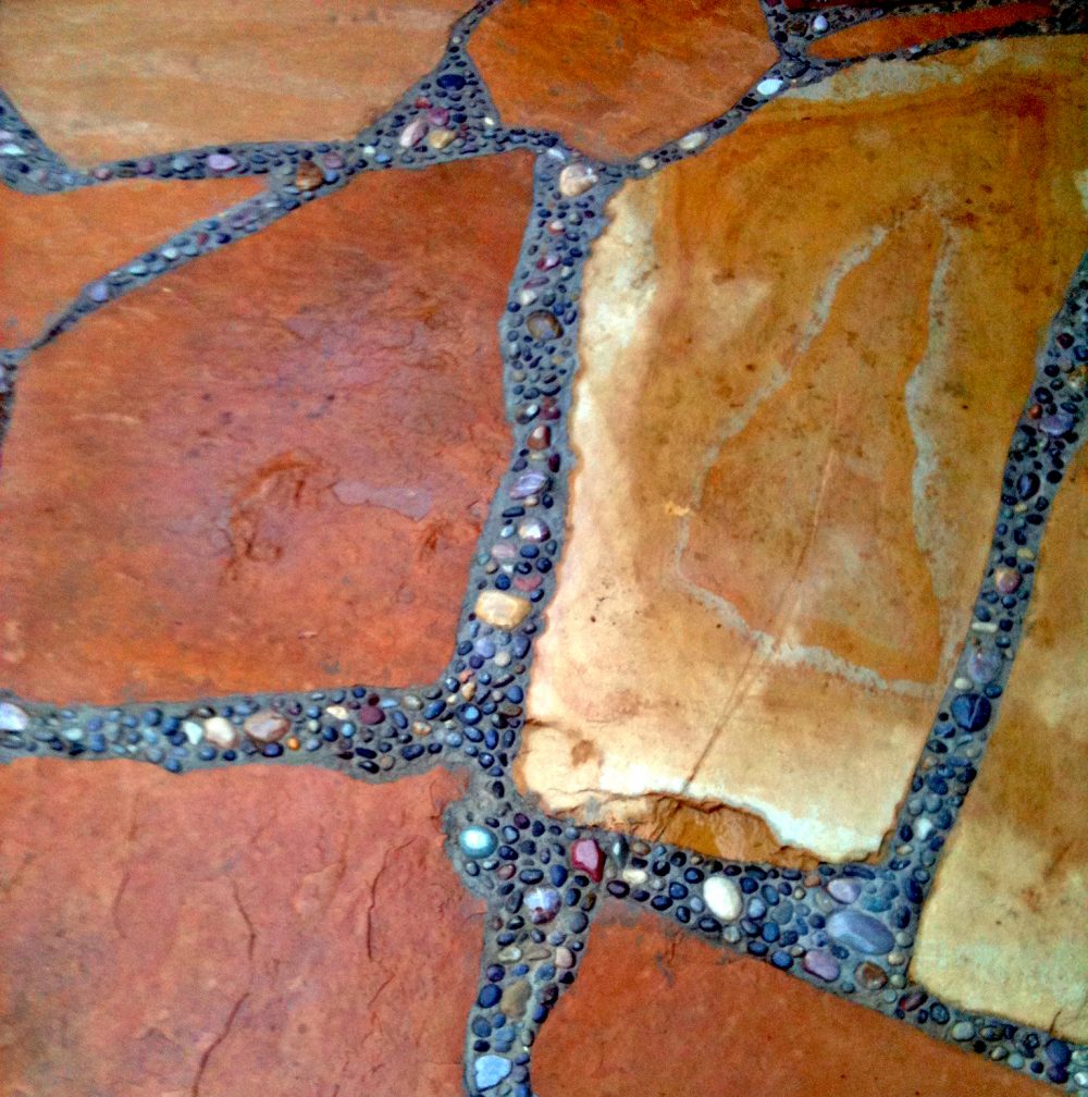 Close up of nine earth-colored patio stones of different shapes and sizes with small colorful pebbles in concrete in between