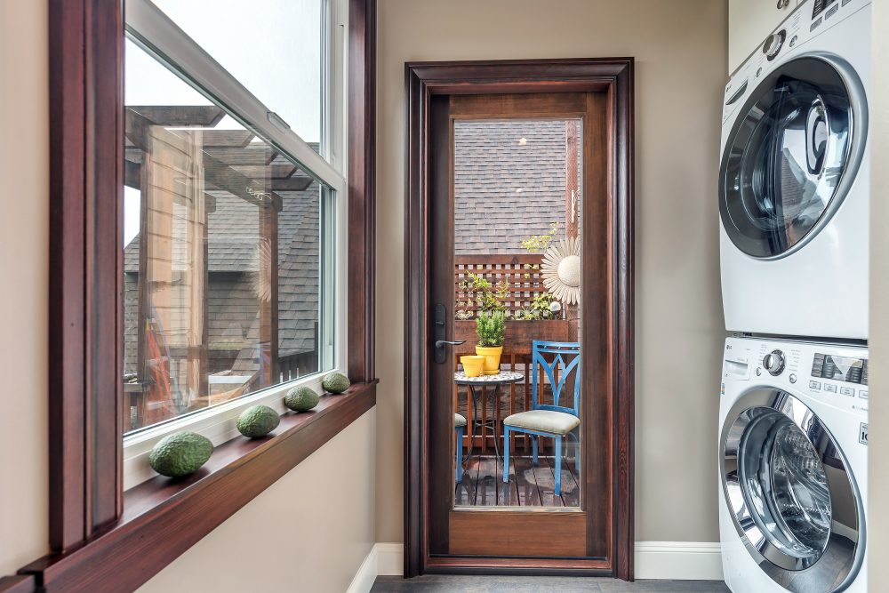 Stacking washer and dryer in laundry room off kitchen area with door leading to yard and wall of windows