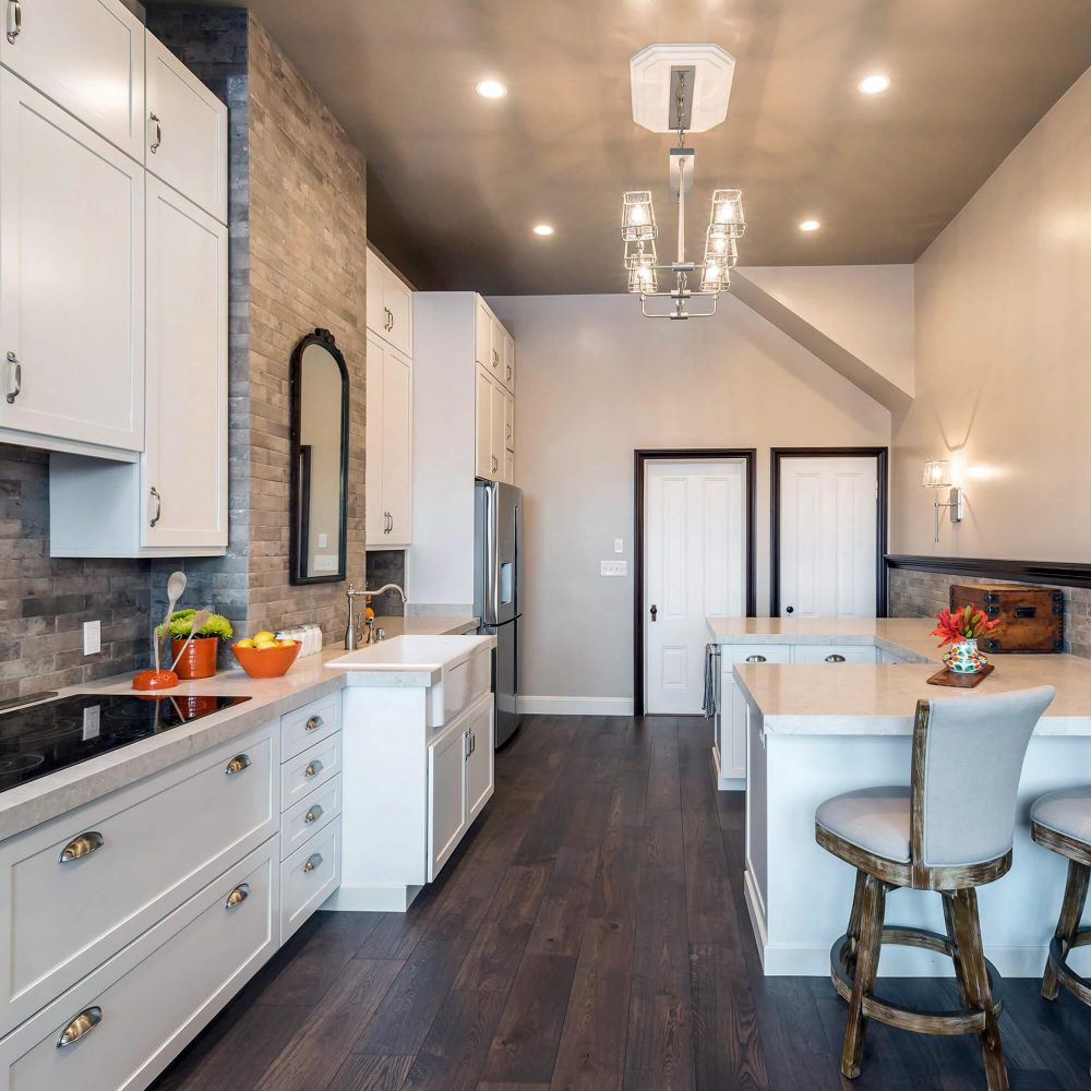 Kitchen stove, sink, counter seating, dark wood floors with white cabinets