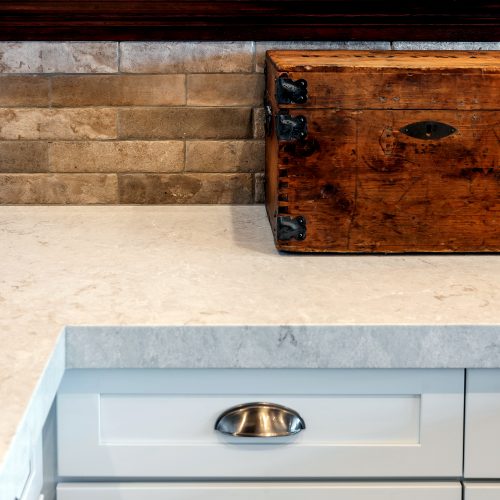 Close up of kitchen cabinet pulls, white marble countertop, stone backsplash, dark wood molding