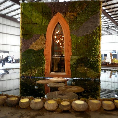 Straight on view of the orange arched door of the plant covered structure with 4 large stepping stone through the water up to the front door