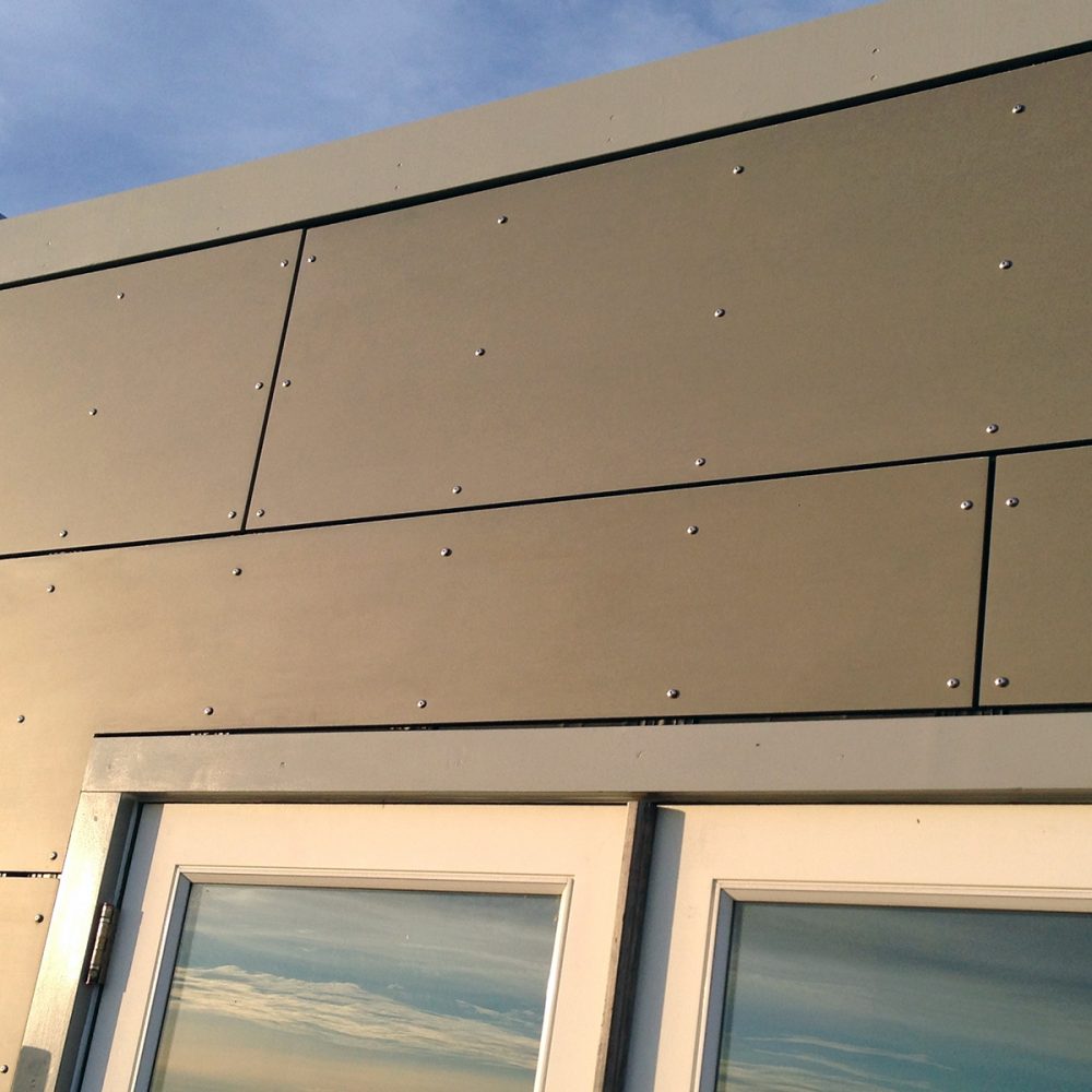 Close up of sand colored man made siding and windows reflecting the sky and clouds