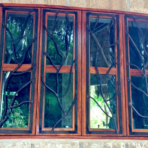 A stone house with four paned vertical window with hinges that open out and customized iron window grill shaped like thin branches