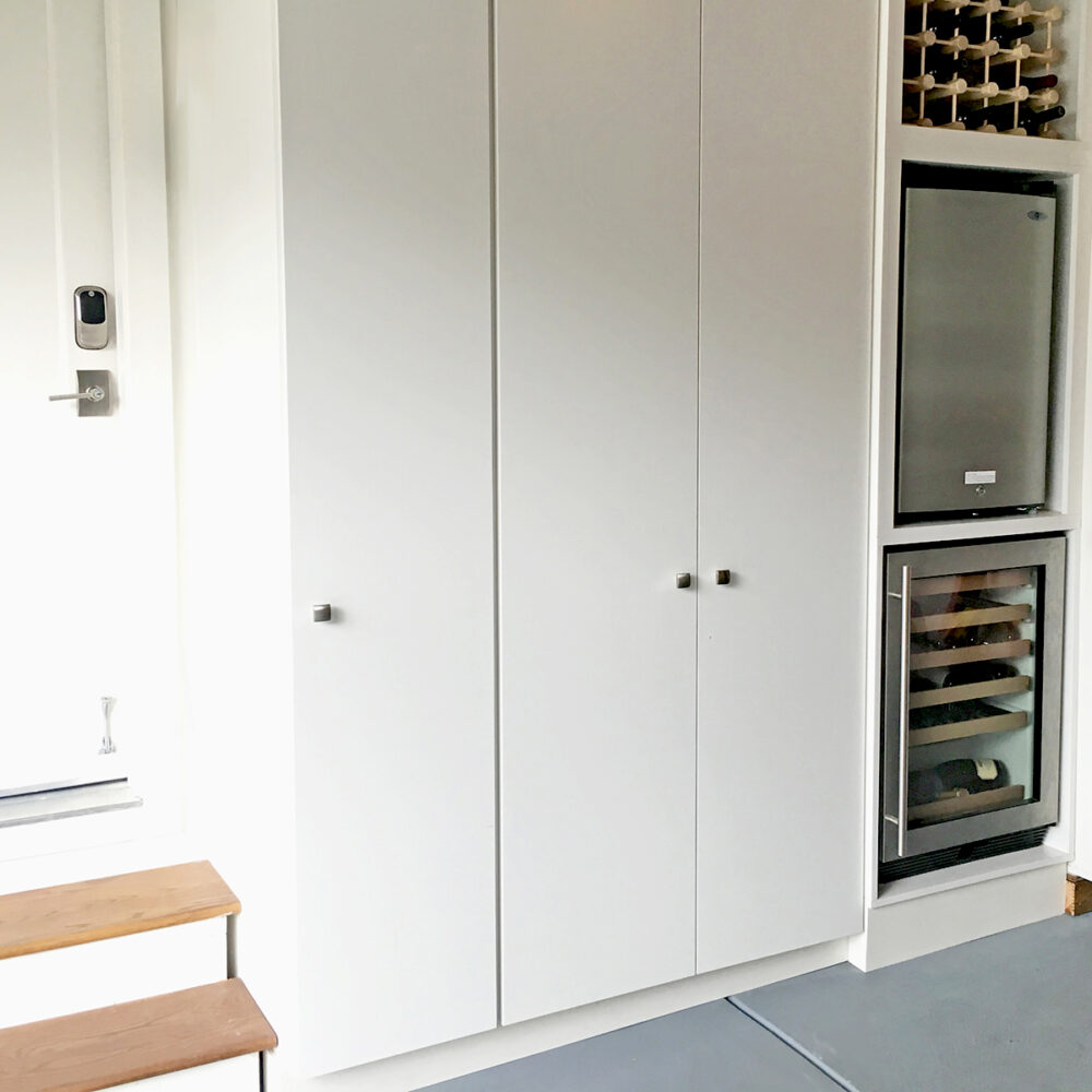 Floor to ceiling enclosed cabinets next to interior door of garage with wine storage, wine cooler, and half fridge