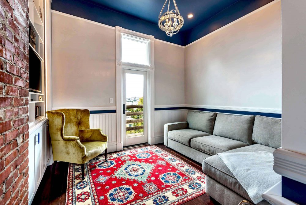 Guest room with door to outside deck, L shaped sofa, large chair, bright rug, and built-ins