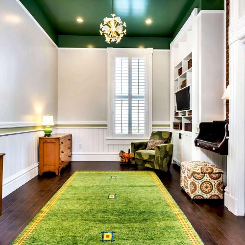 Fair Oaks interior with two wooden dressers, a bright green rug, and chair next to built-in entertainment center and desk